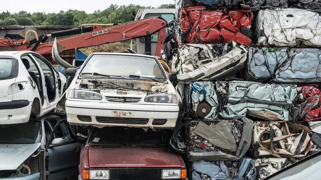 Compressed cubes of crushed car bodies stacked beside intact wrecks at a scrapyard