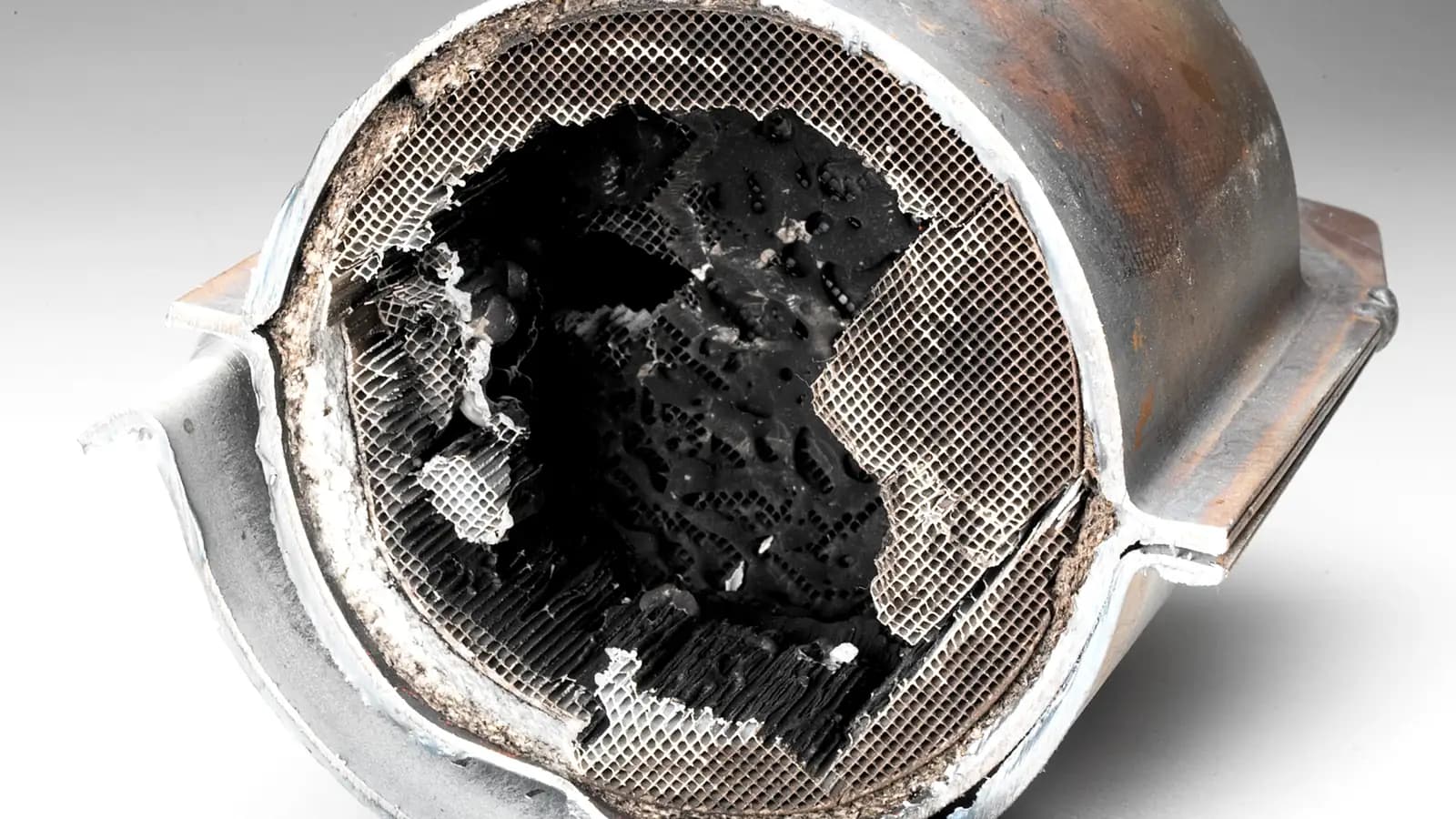 A catalytic converter cut open to show the dark honeycomb core inside its steel case