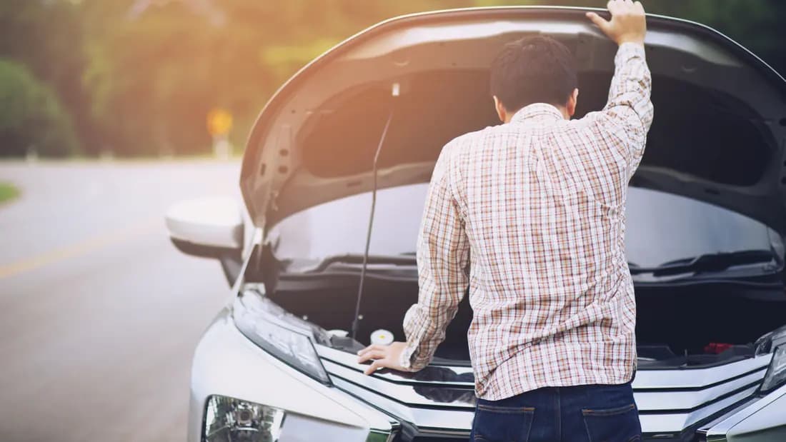 A man looking under the raised bonnet of a car that will not start
