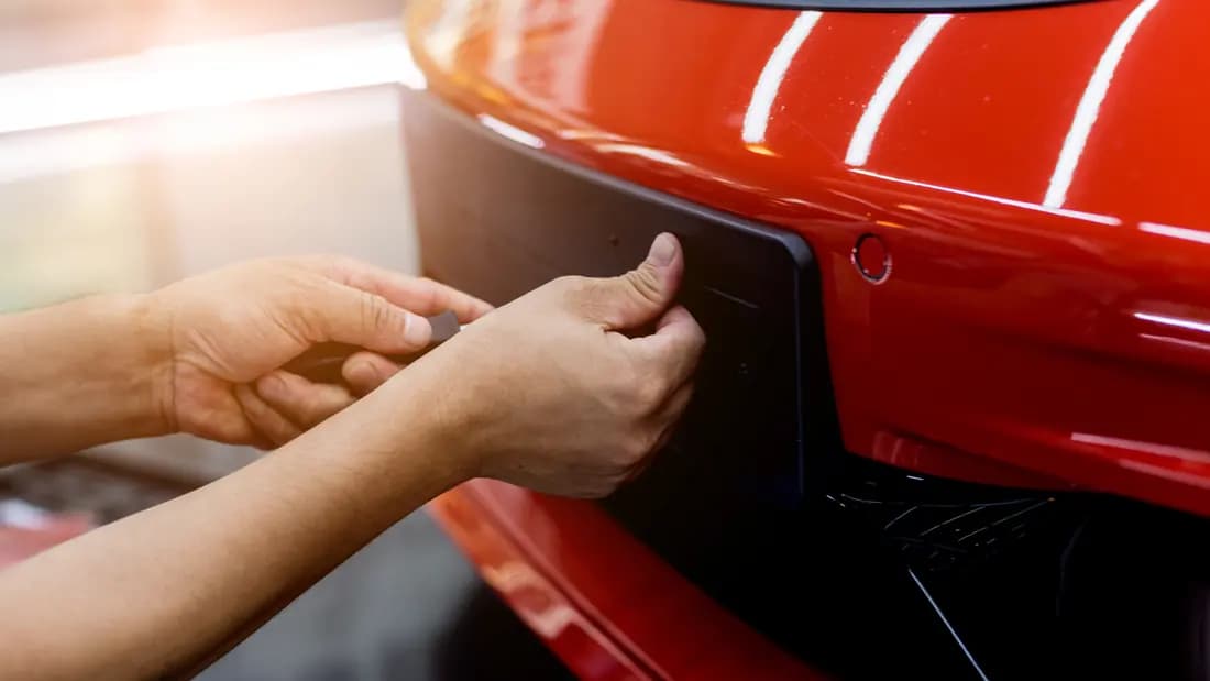 Two hands removing a number plate from the rear of a red car