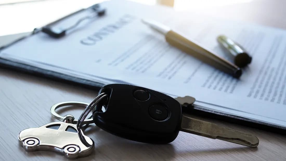 A car key resting on a printed vehicle contract beside a pen and clipboard