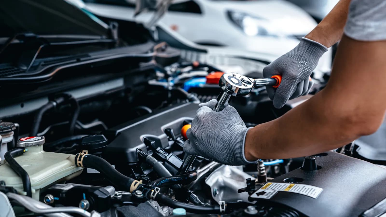 Gloved hands using a ratchet wrench on a car engine under an open hood