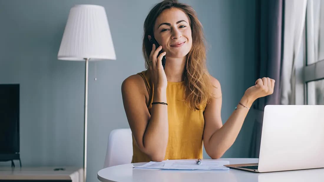 A woman at a table with documents and a notebook, talking on her phone: asking a leasing company for a payoff quote in Nevada