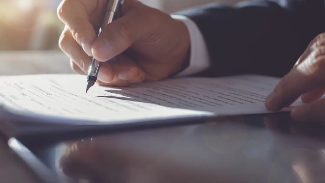 A close view of a hand signing a printed document with a pen on a desk