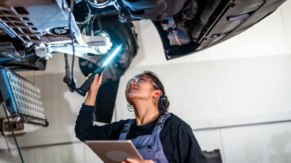 A mechanic inspecting a car's underside with a flashlight and tablet: the Nevada rebuilt title inspection