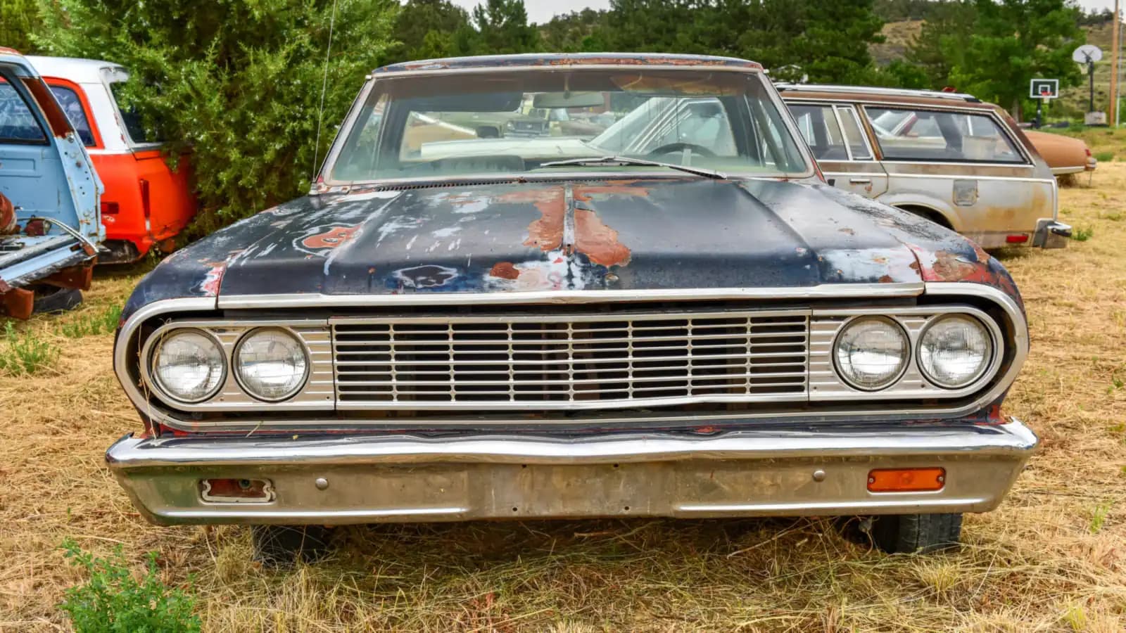 Front of a rusted vintage car with chrome headlights parked in a junkyard: sell to Pick-n-Pull or a car buyer in Nevada
