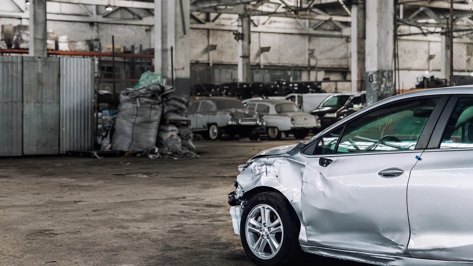A damaged silver car in a repair warehouse with older cars behind it: rebuilt title vs salvage title in Nevada