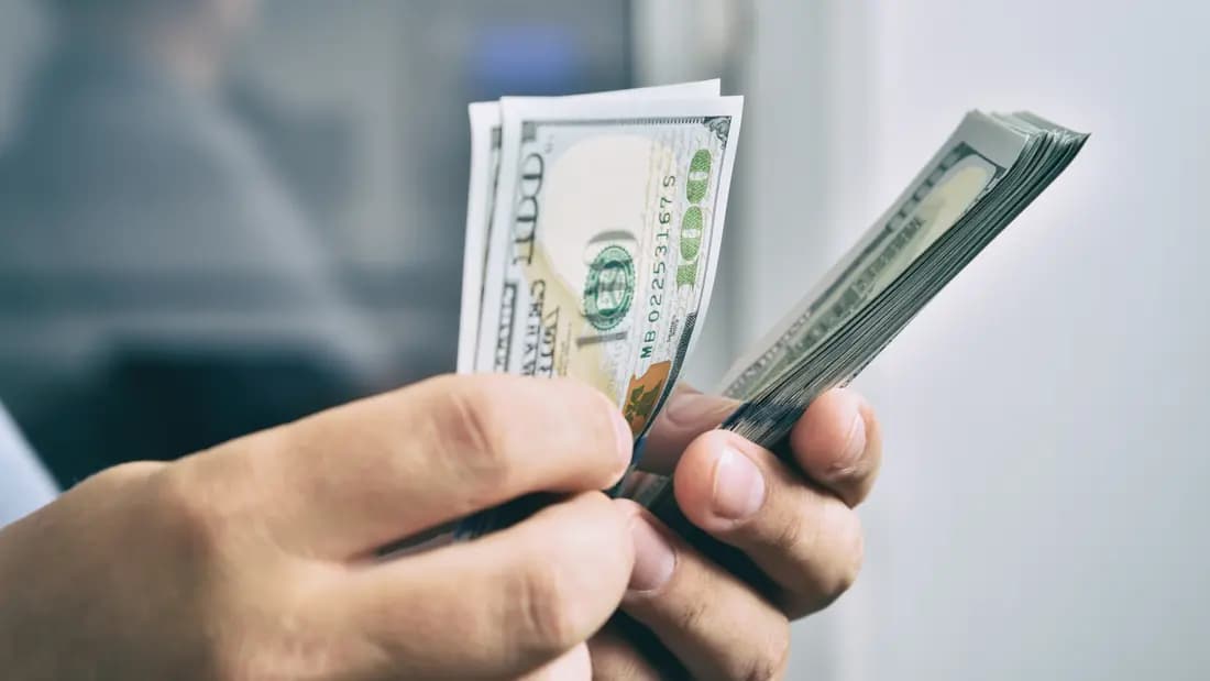 A pair of hands counting a thick stack of US hundred dollar bills