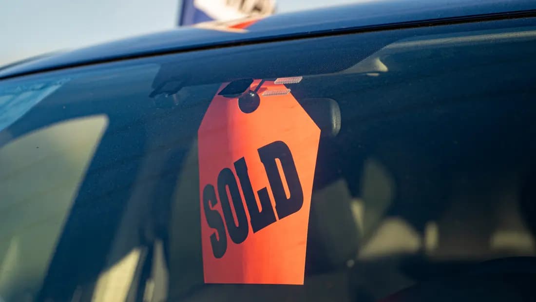 A bright orange SOLD tag hanging inside a car windscreen