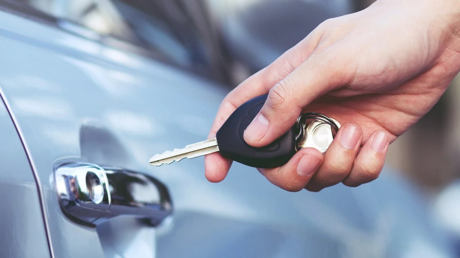 A hand holding a car key beside a car door: sell a car with no keys in Las Vegas and what a buyer needs instead