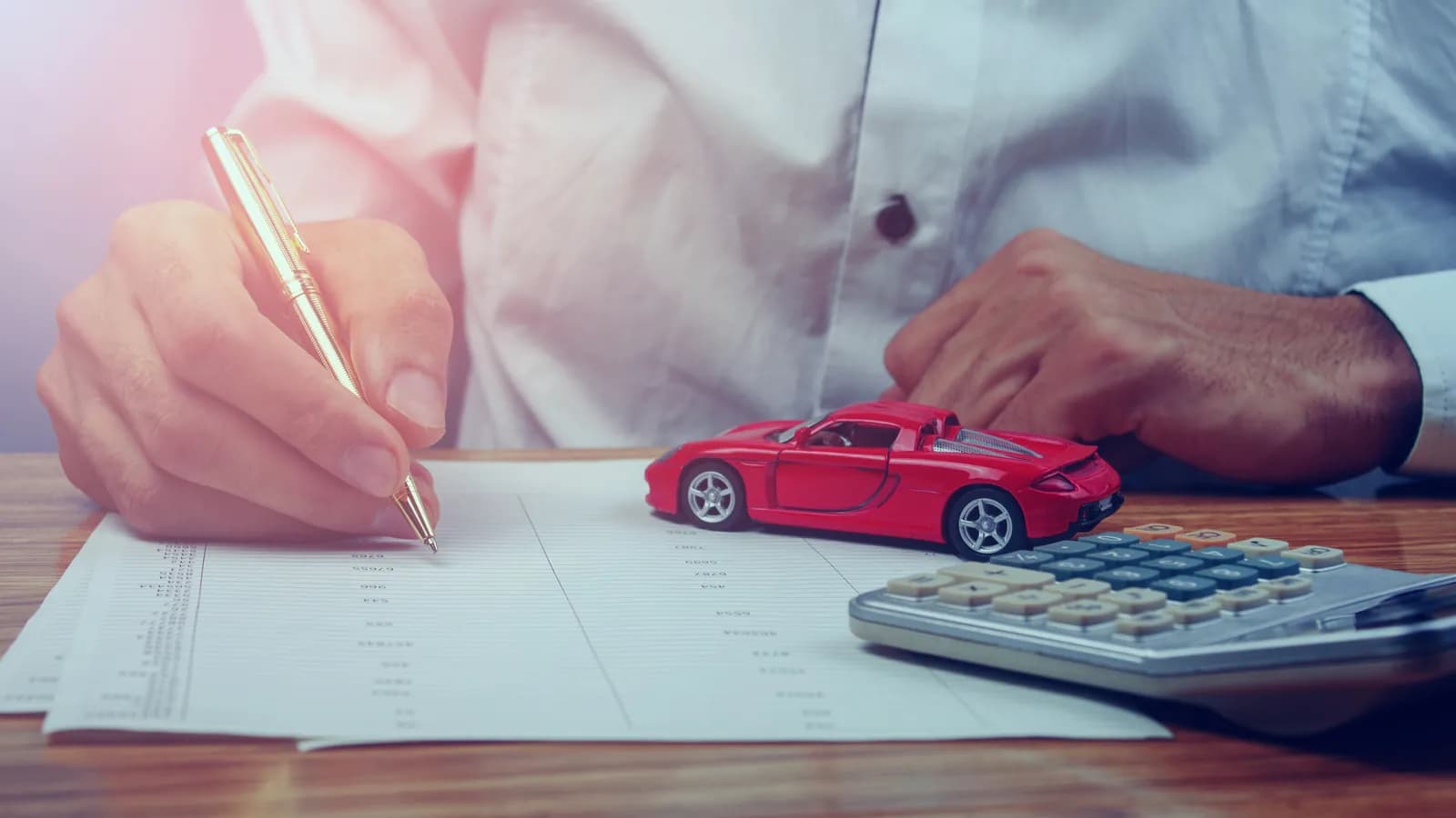 Hand signing a car loan agreement beside a toy car and calculator: sell a financed car in Nevada once the lien is released