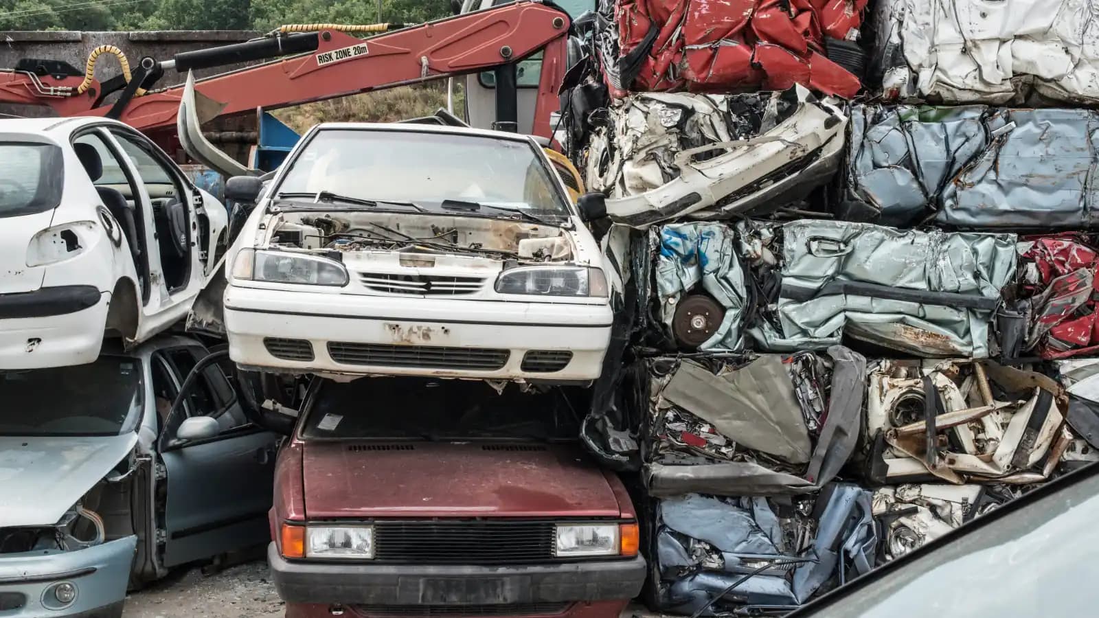 Stripped white and red cars stacked beside crushed car bales at a scrap yard