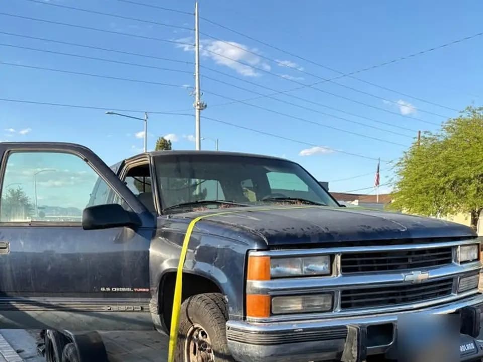Dark blue Chevrolet pickup strapped onto a flatbed trailer, license plate blurred