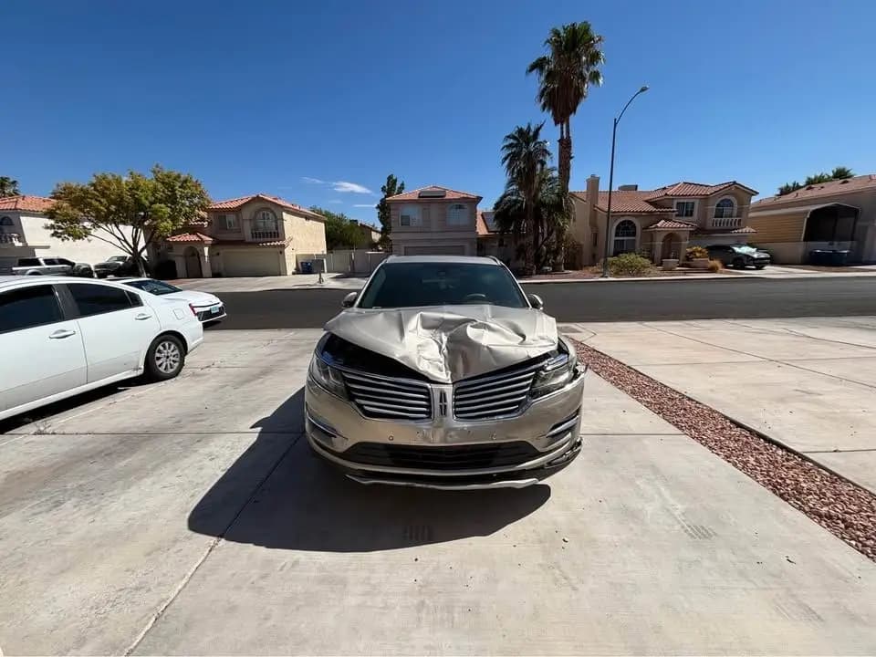 Gold 2015 Lincoln MKC with a crumpled hood parked on a Las Vegas driveway