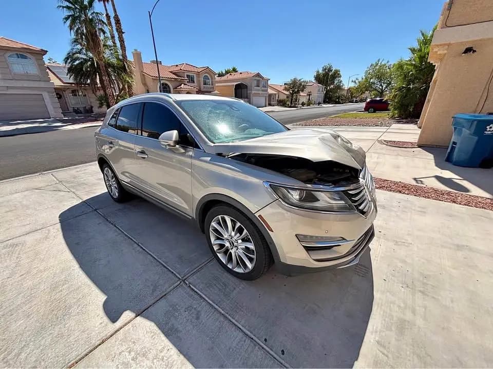 Gold 2015 Lincoln MKC with damage to the headlight, hood and bumper, parked in a driveway