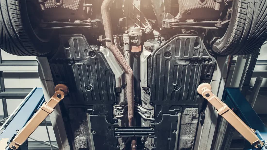 The underside of a car on a lift, where a junk car's value is decided The underside of a car raised on a workshop lift, showing the exhaust, floor pan and suspension