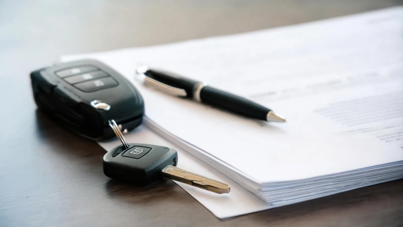Replacing a lost Nevada car title with a duplicate from the DMV Car key fob and ignition key beside a pen on a stack of vehicle paperwork on a dark wooden desk