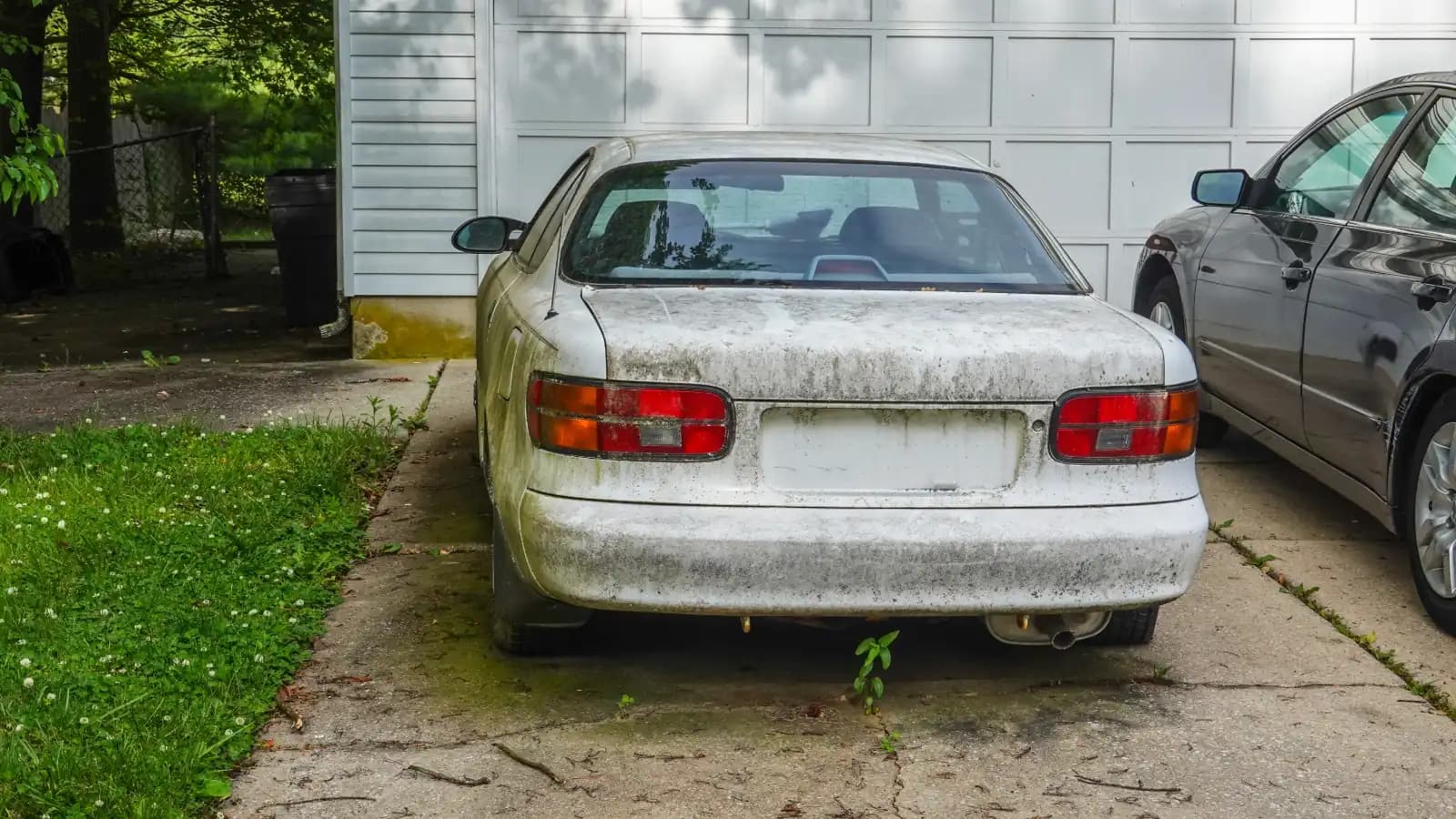 Selling a car with expired registration in Nevada A weathered white sedan with mildew on the paint parked on a cracked driveway beside a garage
