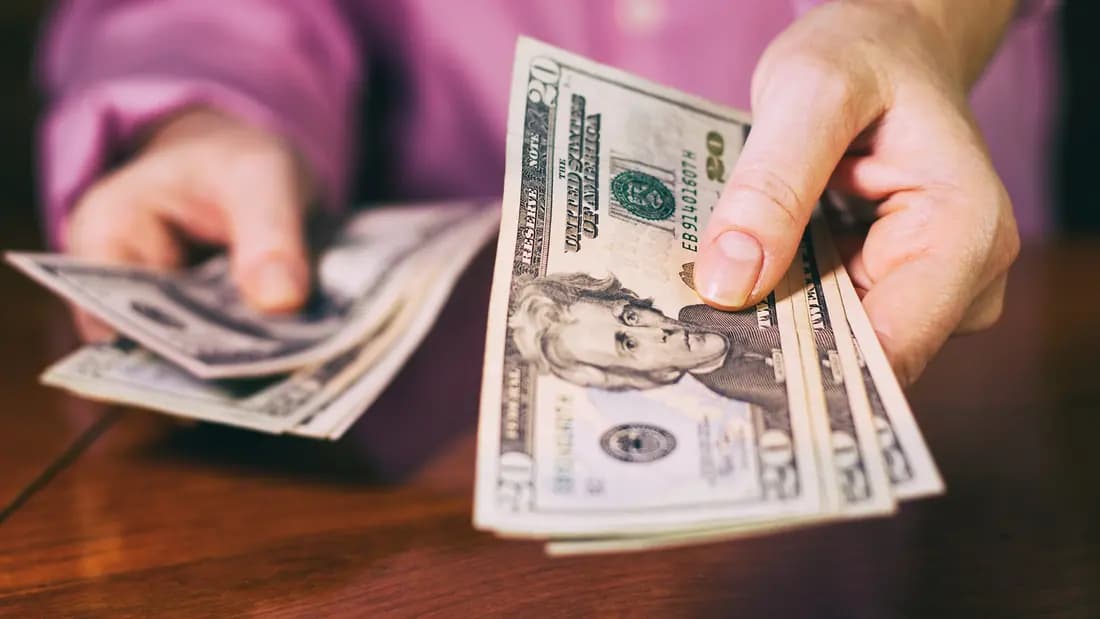 The price drop at pickup, the most common cash for cars scam A person holding out a fan of US twenty and hundred dollar bills across a table