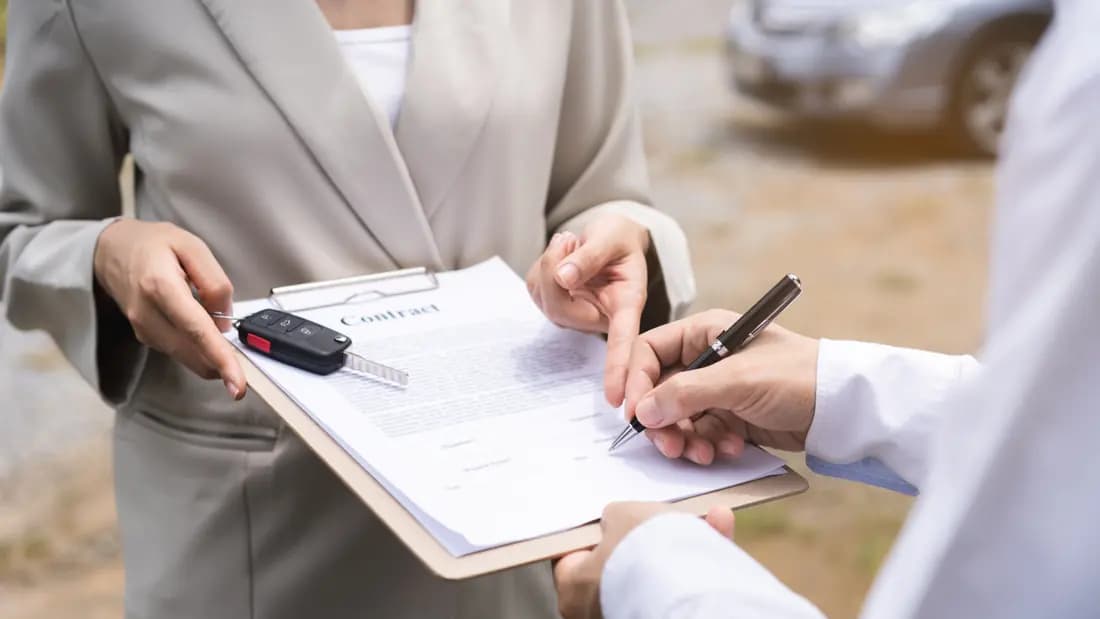 Paperwork that protects you when selling a car for cash Two people signing a vehicle sale document on a clipboard while one holds a car key